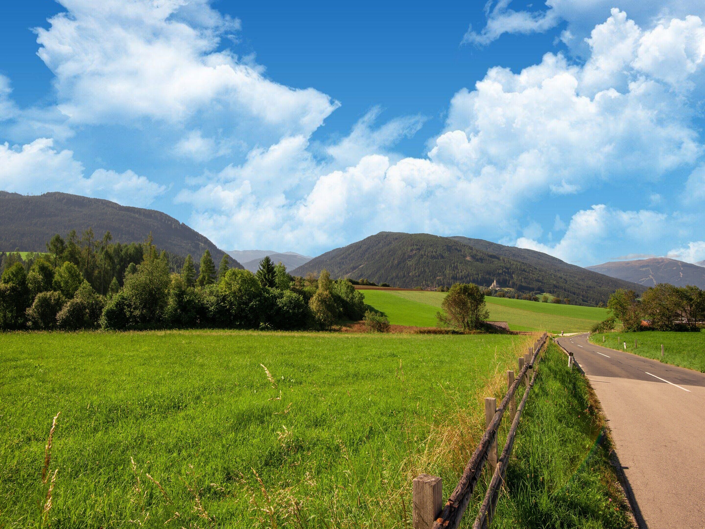 A rural landscape with a road, green fields, and mountains in the background.