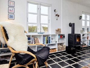 A cozy living room with a large window, a fireplace, and a bookshelf filled with books and decorative items. - 5 Person Holiday Home in Brovst (Brovst)