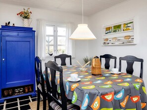 A dining area with a table set for four, featuring a colorful tablecloth with bird patterns, black chairs, and a blue cabinet with shoes underneath. - 5 Person Holiday Home in Brovst (Brovst)