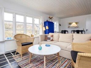 A room with a white sofa, two wicker chairs, a round table with a vase, and a blue cabinet. - 5 Person Holiday Home in Brovst (Brovst)