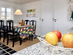 A kitchen with a dining table, chairs, and a fruit basket with apples on a granite countertop. - 5 Person Holiday Home in Brovst (Brovst)
