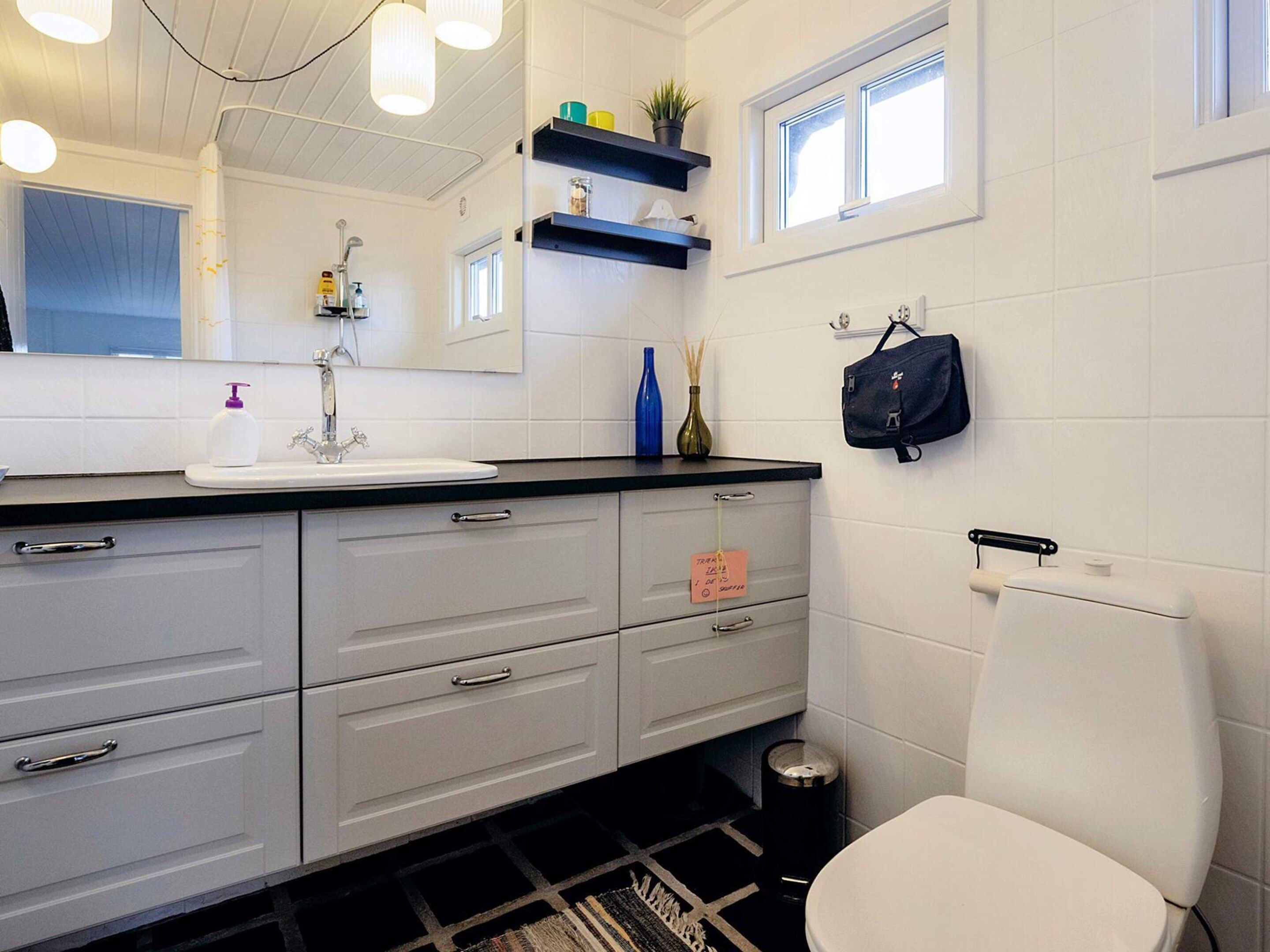 A modern bathroom with a white sink, mirror, and toilet. There are storage cabinets and a small trash bin.
