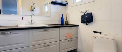 A modern bathroom with a white sink, mirror, and toilet. There are storage cabinets and a small trash bin.