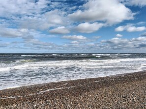 A beach with pebbles, waves, and a partly cloudy sky. - 5 Person Holiday Home in Brovst (Brovst)