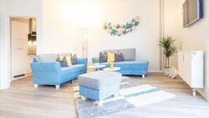 A modern living room with a blue sofa set, a small round coffee table, and a decorative wall piece. - Message in a Bottle Modern Retreat (Zingst)