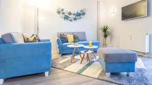A modern living room with two blue sofas, a coffee table, and a small side table. There is a wall-mounted TV and a decorative wall piece. - Message in a Bottle Modern Retreat (Zingst)