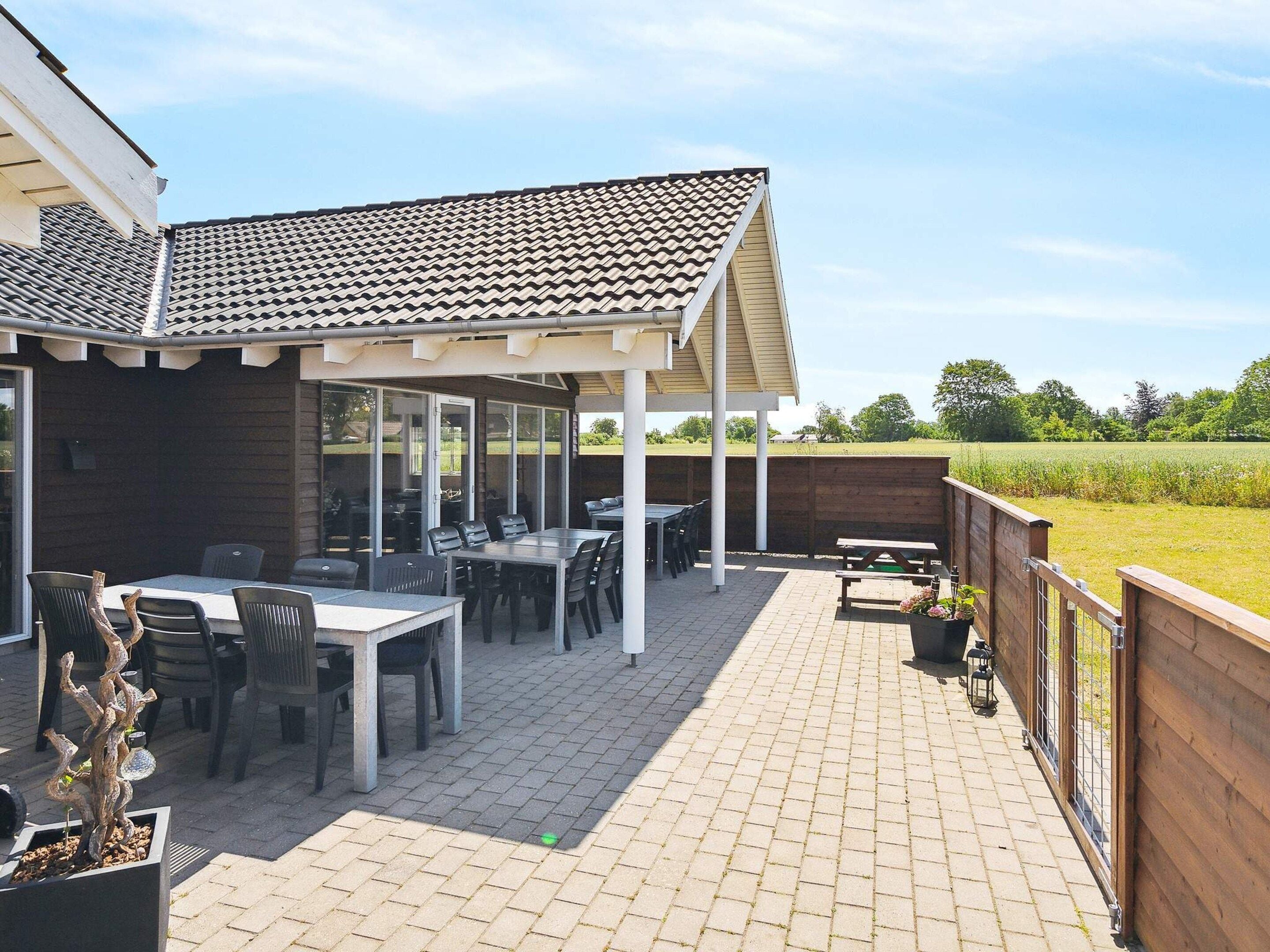 A covered patio area with a table and chairs, a wooden fence, and a view of the countryside.