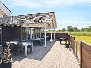 Een overdekt terras met een tafel en stoelen, een houten schutting en uitzicht op het landschap.
