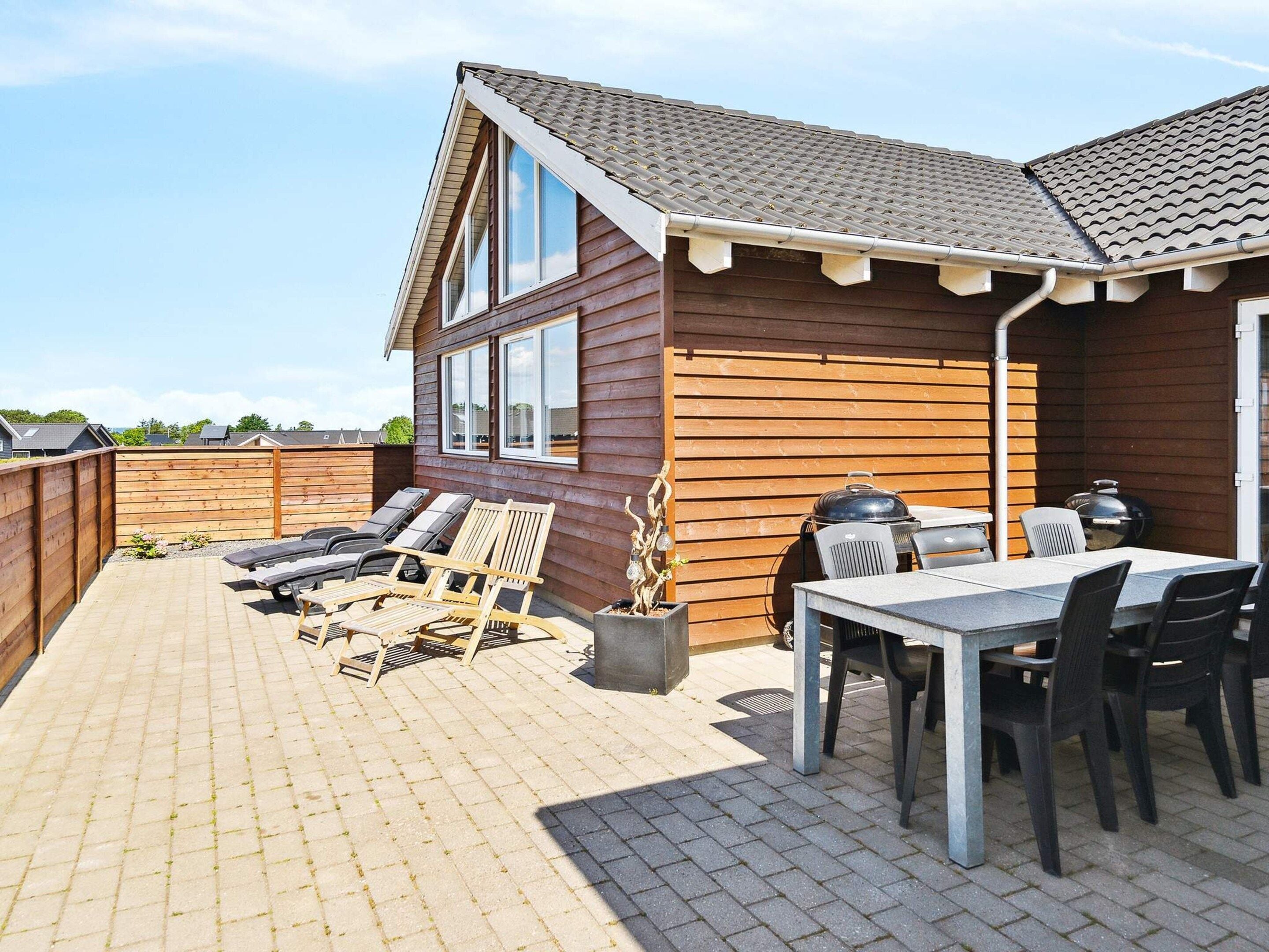 A wooden house with a tiled roof, a patio with a table and chairs, and a barbecue grill.