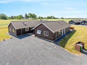 A two-story building with a sloped roof, a gravel driveway, and a grassy field in the background.