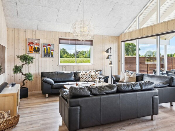 A modern living room with a black leather sofa, a wooden coffee table, and a large window offering a view of the outdoors.