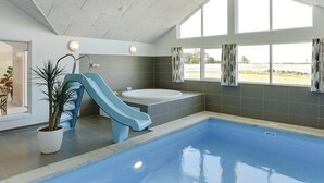 A modern indoor swimming pool with a slide, a jacuzzi, and a view of the outdoors. - 5 Star Holiday Home in Bogense (Bogense)