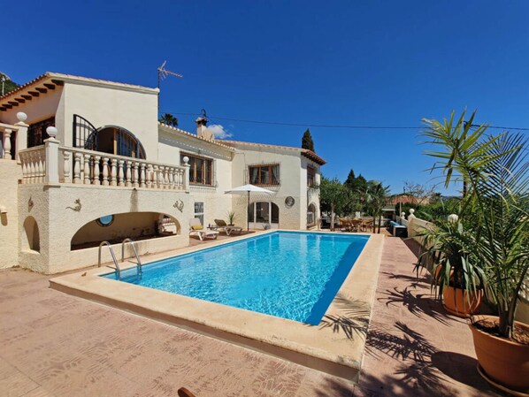 A poolside view of a Mediterranean-style villa with a swimming pool, outdoor seating, and potted plants. - Villa Fiorida Comfortable Holiday Residence (Calpe)
