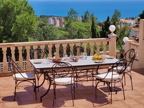 A terrace with a table set for dining, surrounded by chairs, overlooking a coastal view with buildings in the distance. - Villa Fiorida Comfortable Holiday Residence (Calpe)
