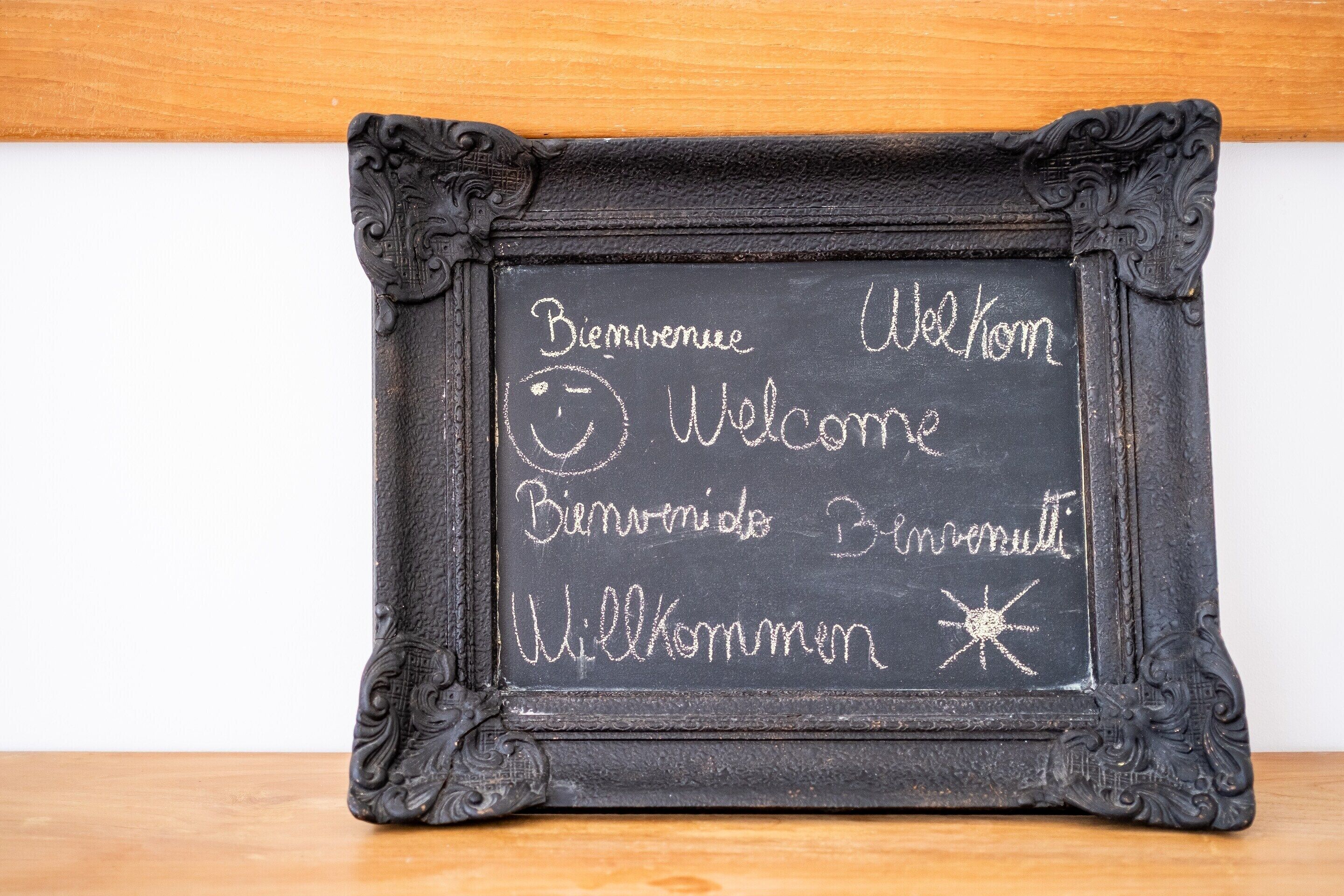 A black chalkboard with "Bienvenue Welcome Bienvenidos Bienvenuti Willkommen" written in multiple languages.