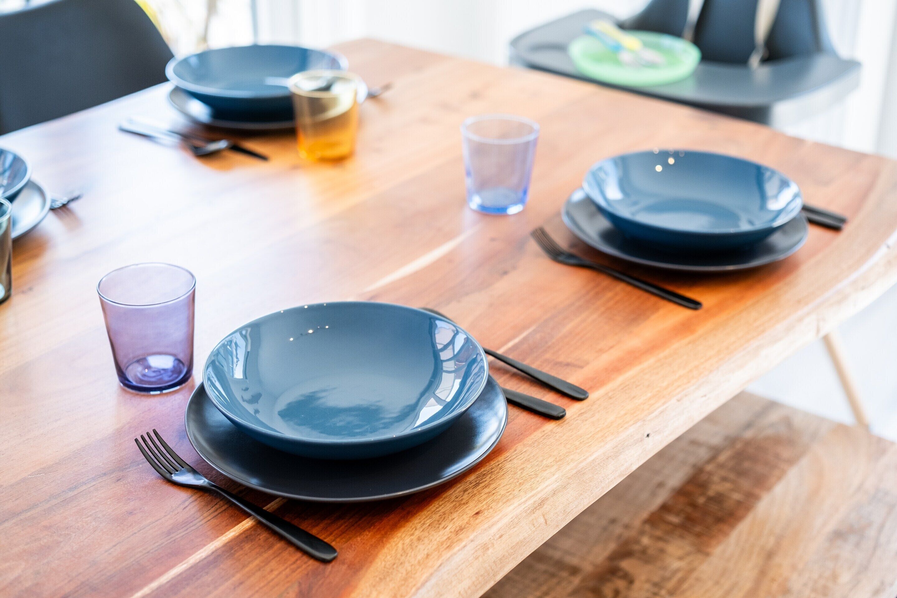 A dining table with blue plates, black cutlery, and a glass of water.