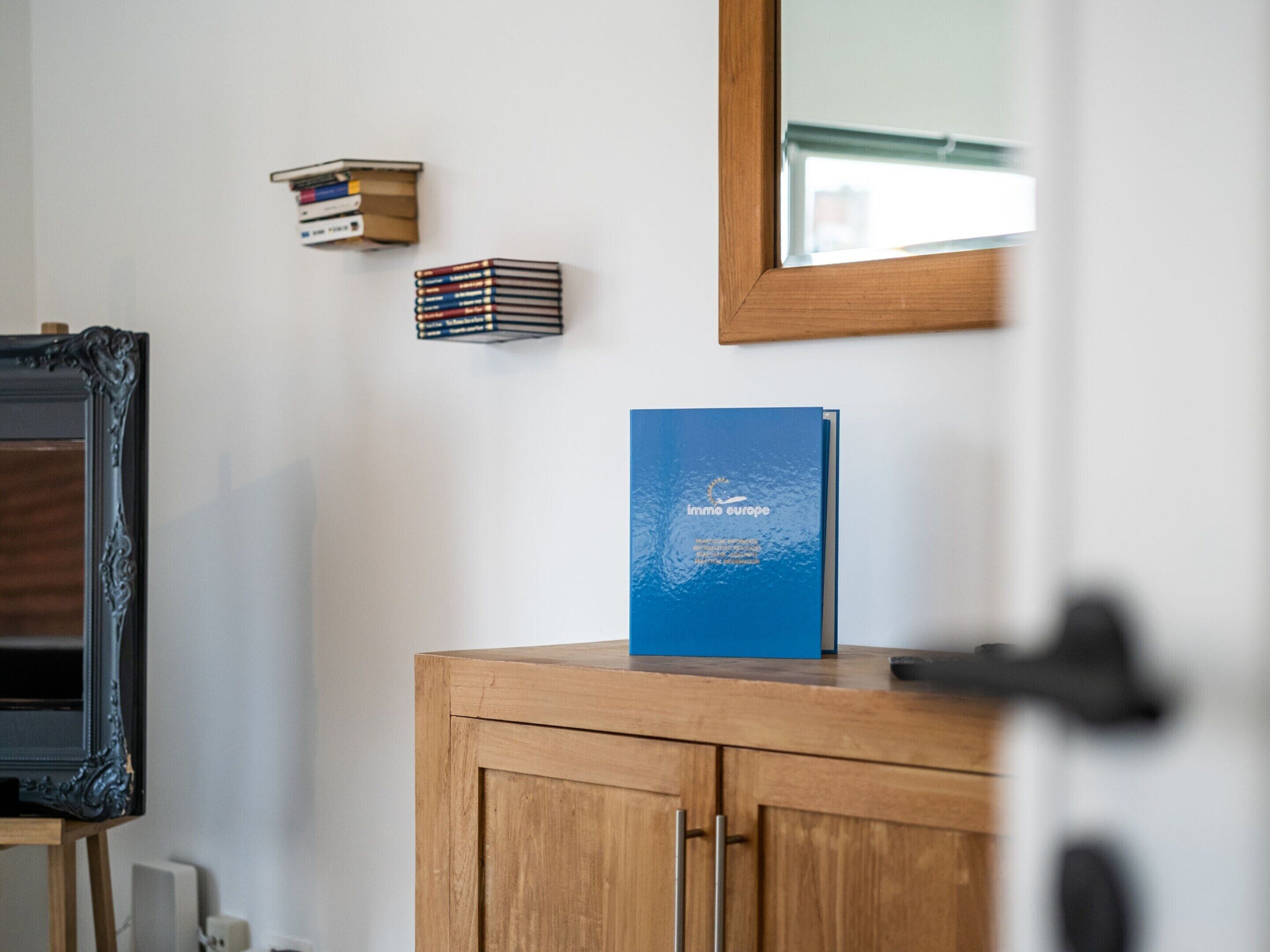 Una habitación con un armario de madera, un espejo y un libro azul titulado 'Immo Europe' encima del armario.