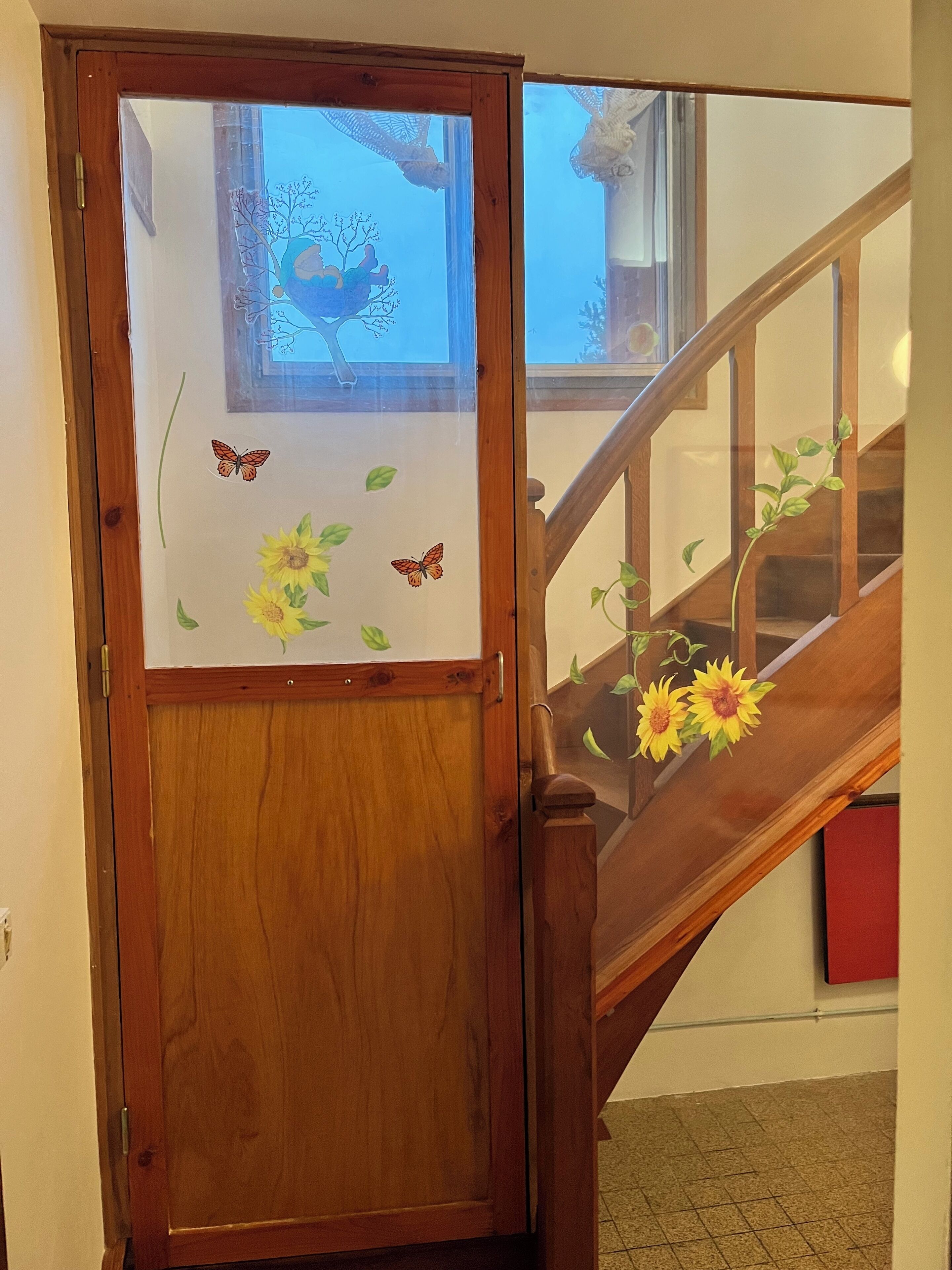 A wooden staircase with a glass door featuring a butterfly and sunflower decal.