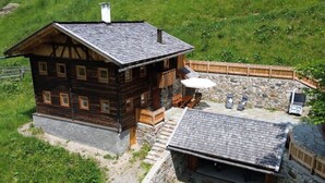 Eine Holzhütte mit Steinfundament, einem Balkon mit Sitzgelegenheit und einer Steinmauer, die die Terrassenfläche umgibt.
