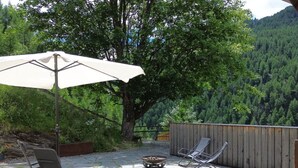 Eine Außenpatio mit Steinböden, einer Feuerstelle, zwei Loungestühlen und einem großen Sonnenschirm.