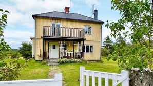 Une maison en bois à deux étages, dotée d’un balcon, d’une porte d’entrée et d’un petit porche.