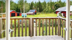 Une terrasse en bois offrant une vue sur un paysage rural, avec notamment des granges rouges et une petite maison de jeu bleue.