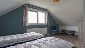 Huone, jossa on kalteva katto, valkoisilla vuodevaatteilla varustettu sänky, sininen tuoli ja patteri.