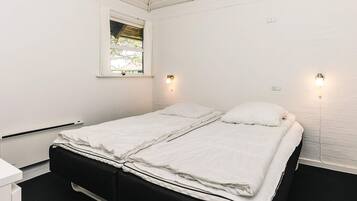 A single bed with white bedding in a room with white walls and a window.