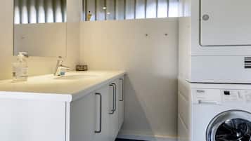 Een kleine, moderne badkamer met een wastafel, spiegel en een gestapelde wasmachine.