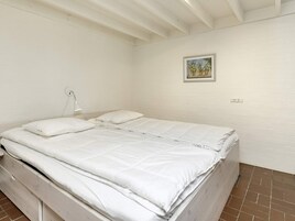 Habitación con cama individual, ropa de cama blanca, lámpara de noche y un pequeño cuadro enmarcado en la pared.