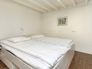 Een eenpersoonskamer met wit beddengoed, een bedlampje en een klein fotokader aan de muur.