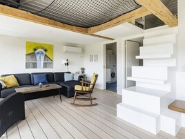 A modern living room with a dark grey sofa, a wooden rocking chair, and a white staircase.