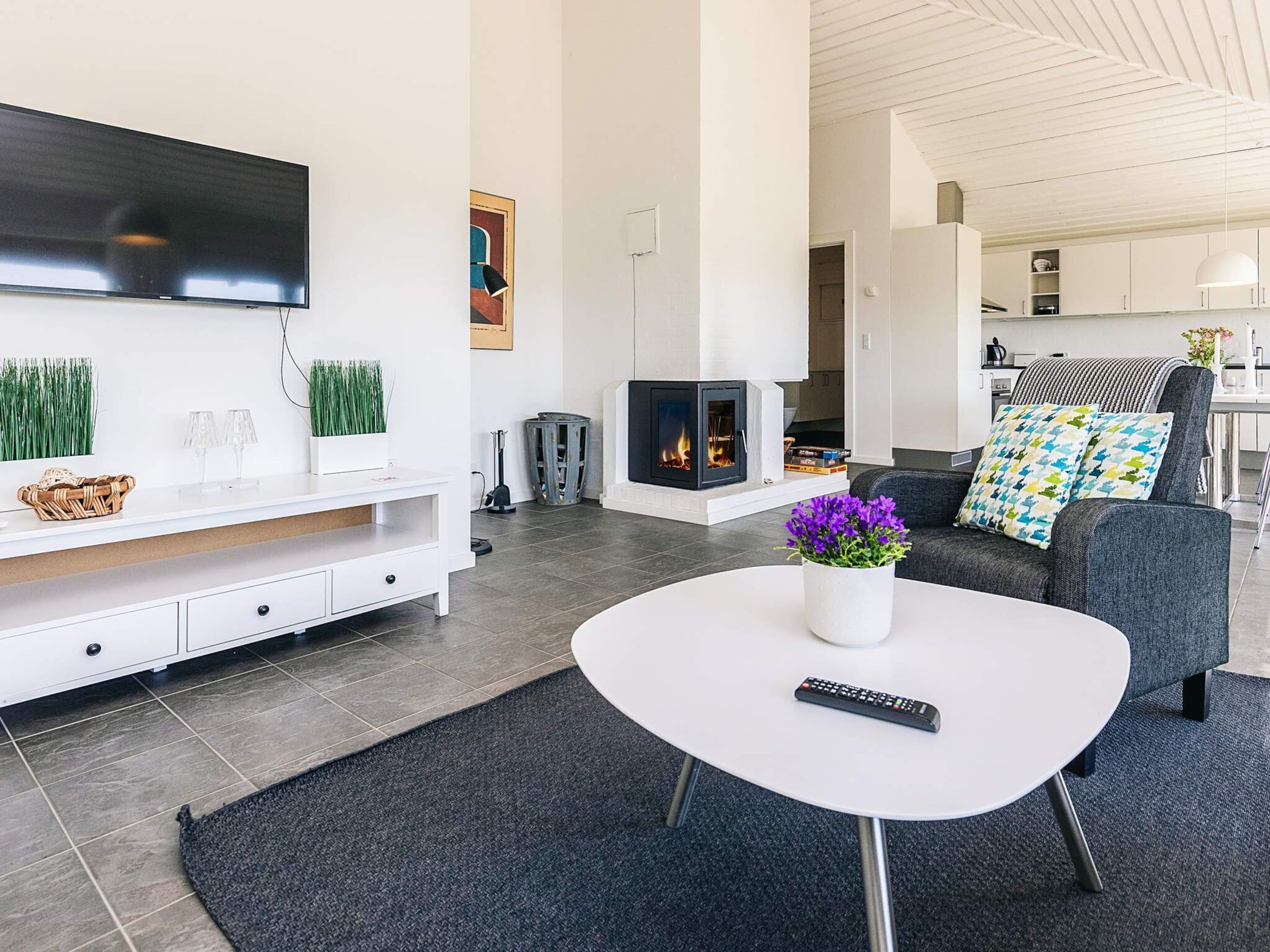 A modern living room with a flat-screen TV, a fireplace, a sofa with patterned cushions, and a coffee table with a vase of flowers.