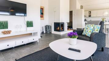 A modern living room with a flat-screen TV, a fireplace, a sofa with patterned cushions, and a coffee table with a vase of flowers.