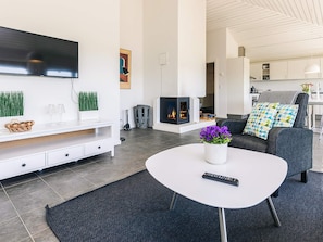 A modern living room with a flat-screen TV, a fireplace, a sofa with patterned cushions, and a coffee table with a vase of flowers. - 5 Person Holiday Park Home in Karrebaeksminde (Karrebæksminde)