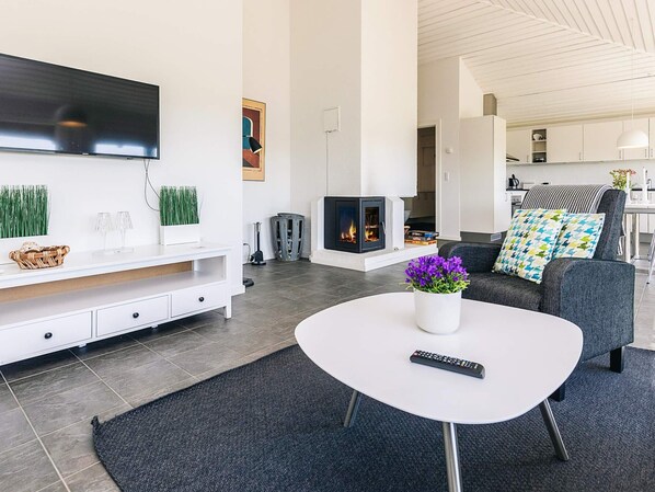 A modern living room with a flat-screen TV, a fireplace, a sofa with patterned cushions, and a coffee table with a vase of flowers.