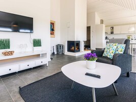 Una sala de estar moderna con una televisión de pantalla plana, una chimenea, un sofá con cojines estampados y una mesa de centro con un jarrón de flores.