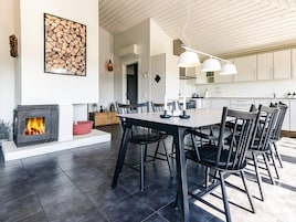 A modern kitchen with white cabinets, a dining area with a large table and chairs, and a fireplace with a visible fire.