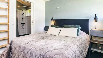 Un dormitorio con una cama grande, un cabecero, dos lámparas de noche, una mesita de noche y una puerta que da a un baño con ducha.
