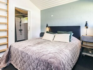 Ein Schlafzimmer mit einem großen Bett, einem Kopfteil, zwei Nachttischlampen, einem Nachttisch und einer Tür zu einem Badezimmer mit Dusche.