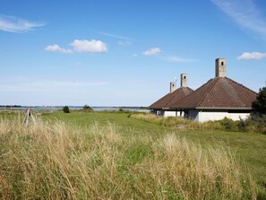 A traditional building with a tiled roof and chimneys, situated in a grassy field with a clear sky and distant water body. - 5 Person Holiday Park Home in Karrebaeksminde (Karrebæksminde)