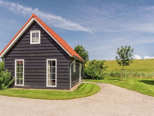A dark wooden house with a red roof and white windows, surrounded by a well-maintained lawn and a gravel driveway.