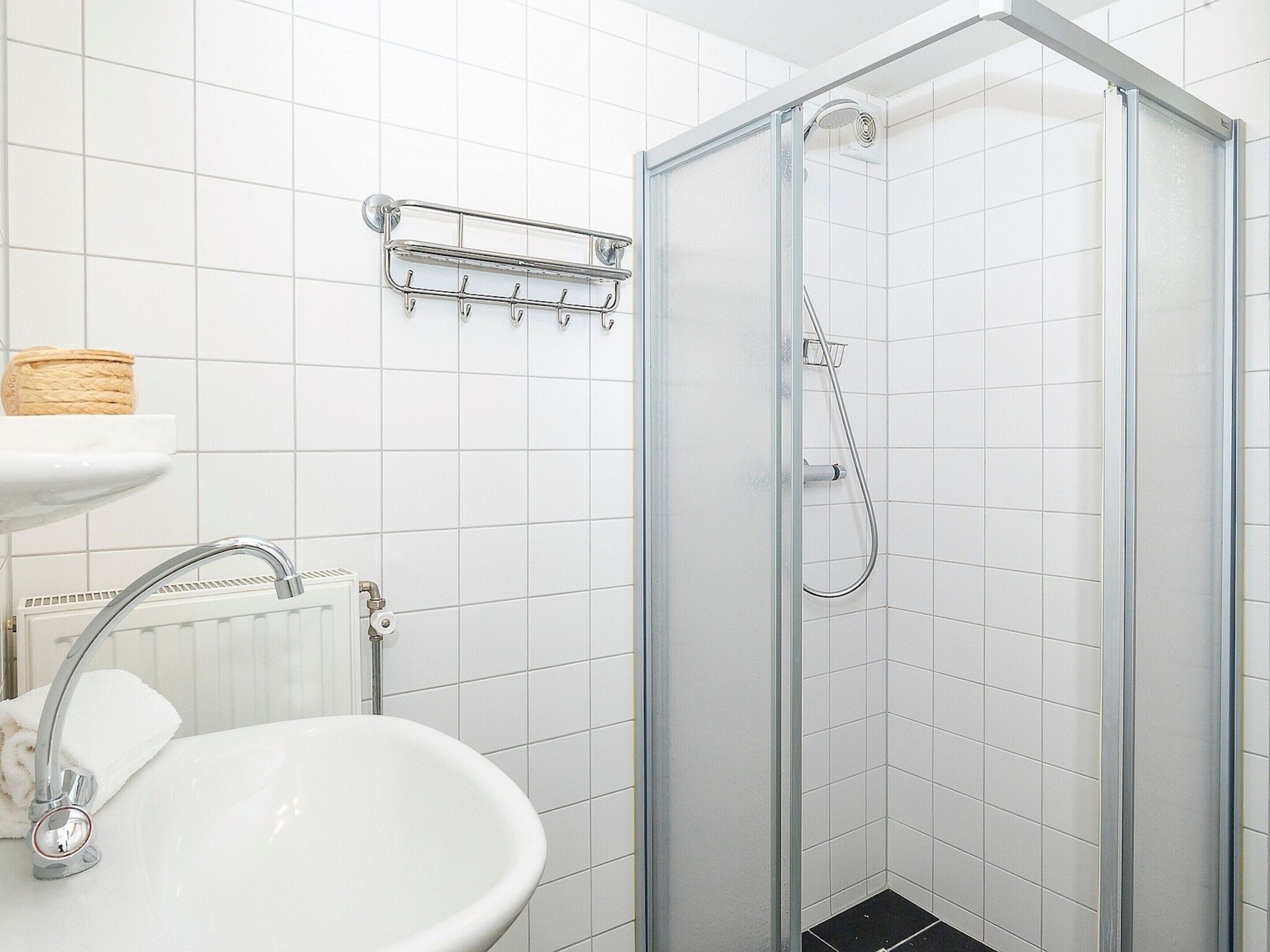 Un baño con ducha de vidrio, lavamanos blanco y barra para toallas.