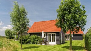 A two-story wooden house with a red-tiled roof, a small patio with a table and chairs, and a well-maintained lawn.