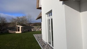 A white building with a thatched roof and a small wooden structure in the yard. - Small Boulder Comfortable Vacation Home (Rerik)