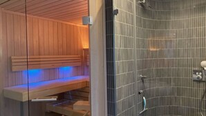 A modern bathroom with a wooden sauna bench, a glass shower enclosure, and a tiled wall. - Small Boulder Comfortable Vacation Home (Rerik)
