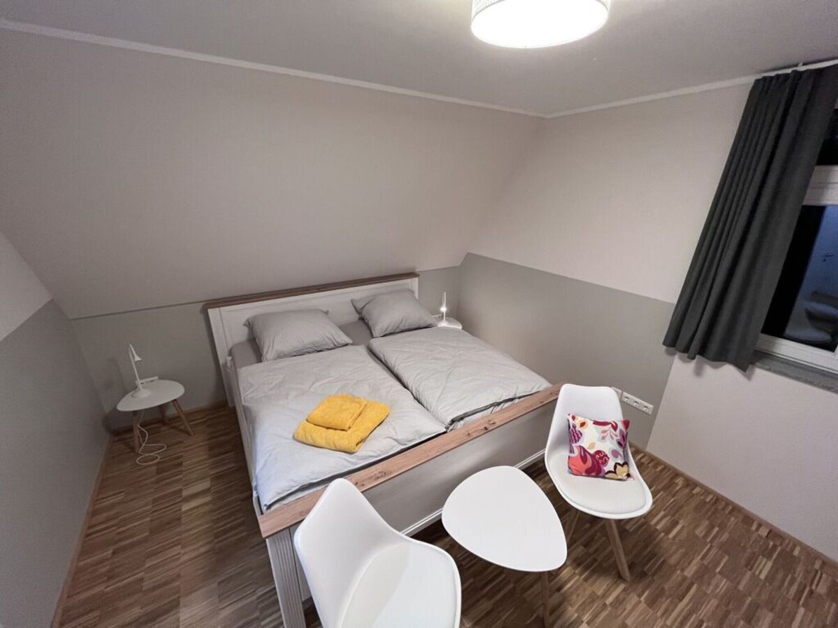 A small, modern bedroom with a bed, bedside tables, and a window with curtains.
