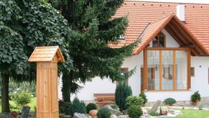 A house with a red-tiled roof, a wooden mailbox, and a well-maintained garden with various plants and a bench. - Apartment Adlerhorst - Schwalbenhof Farm (Sankt Stefan im Rosental)