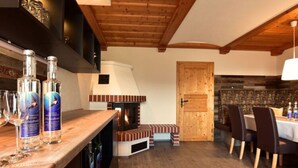 A cozy interior with a wooden ceiling, a fireplace, a dining area with chairs, and a bar with bottles. - Apartment Adlerhorst - Schwalbenhof Farm (Sankt Stefan im Rosental)