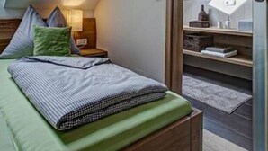 A bedroom with a sloped ceiling, a bed with pillows, a nightstand, and a wooden wardrobe. - Apartment Adlerhorst - Schwalbenhof Farm (Sankt Stefan im Rosental)